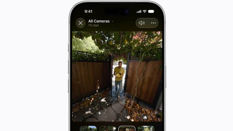 A smartphone screen displays HomeKit Secure Video camera footage of a person standing outside a wooden gate, surrounded by trees and leaves, with video clip thumbnails shown at the bottom.