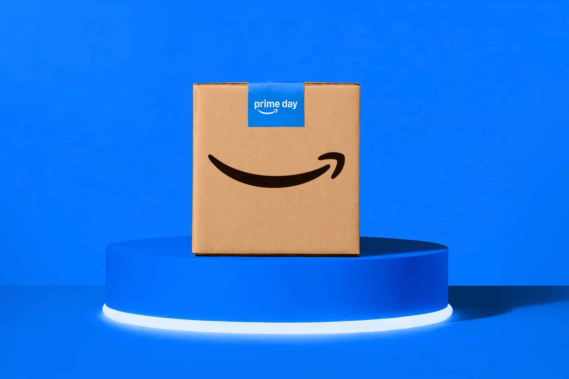 A cardboard box with the Amazon smile logo and a blue "prime day" label sits on a glowing blue pedestal, ready to deliver the new iPhone 17 Pro, against a solid blue background.