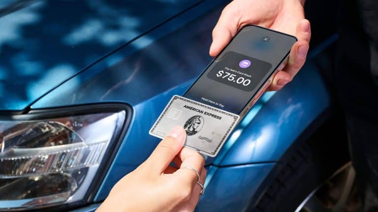 A person holds an American Express credit card near a smartphone displaying a $75.00 payment screen in Apple Wallet, with a blue car in the background, suggesting a contactless payment transaction.