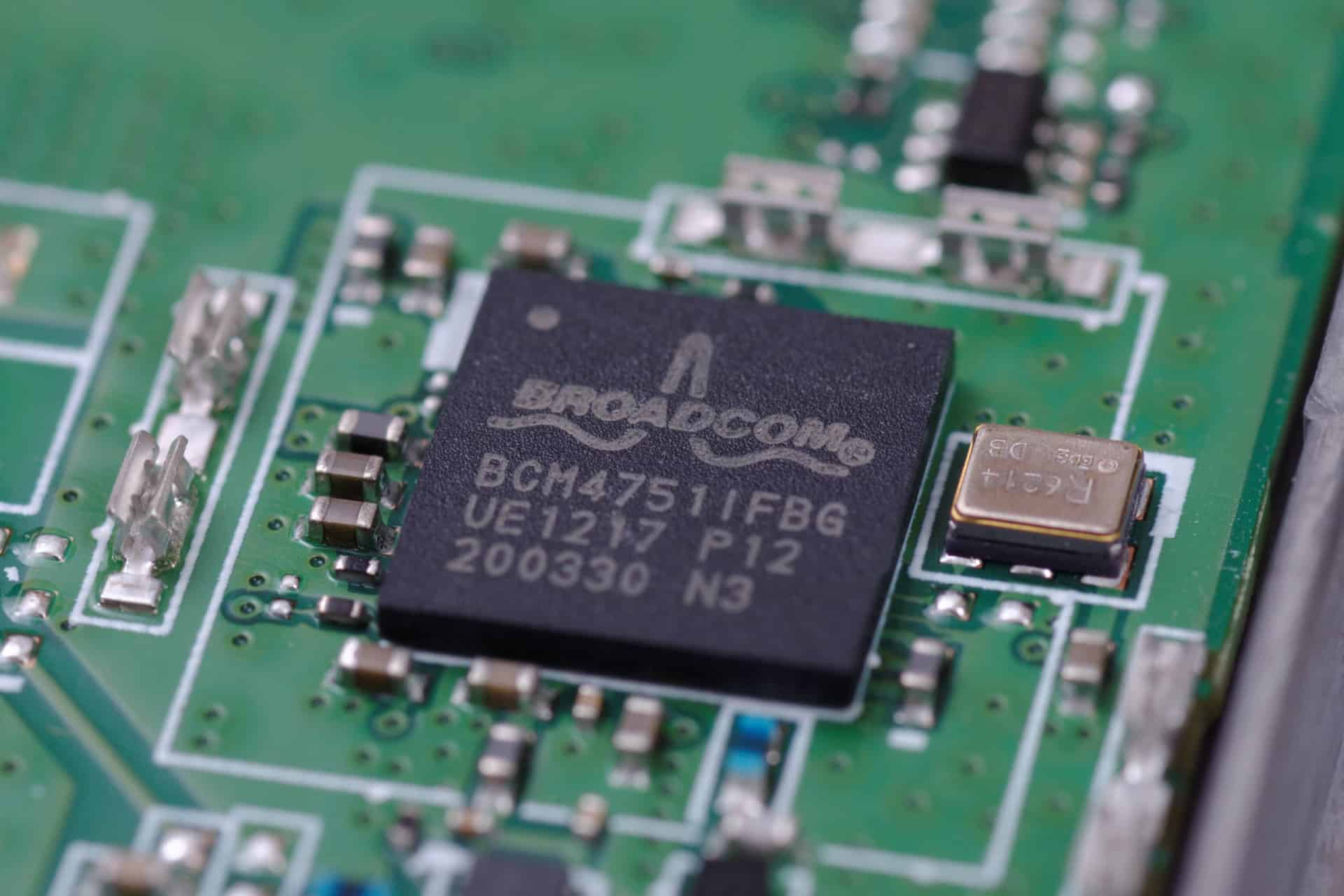 Close-up of a green circuit board featuring a Broadcom BCM47511FBG microchip, highlighting cutting-edge U.S. chip manufacturing alongside various electronic components and visible circuitry.