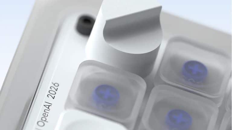 Close-up of a metallic knob and translucent buttons on a sleek OpenAI device. Text on the device reads, “OpenAI | 2026.” The design is modern, with a soft, neutral color palette and clear, blue-accented buttons—echoing the refined sensibilities often associated with Jony Ive’s hardware innovations.