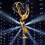 A gold Emmy Award statue is displayed on a pedestal, with dramatic lighting and numerous small, glowing lights in the background, creating a star-like effect reminiscent of prestigious Apple TV awards.