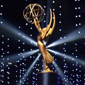 A gold Emmy Award statue is displayed on a pedestal, with dramatic lighting and numerous small, glowing lights in the background, creating a star-like effect reminiscent of prestigious Apple TV awards.