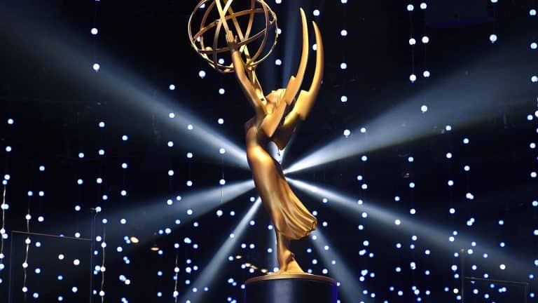 A gold Emmy Award statue is displayed on a pedestal, with dramatic lighting and numerous small, glowing lights in the background, creating a star-like effect reminiscent of prestigious Apple TV awards.