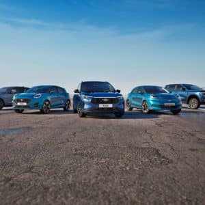 Five blue Ford vehicles, including an electric pickup, are parked in a semi-circle on an empty road under a clear blue sky, with open landscape in the background—showcasing the future of driving with features like Ford Apple Maps integration.