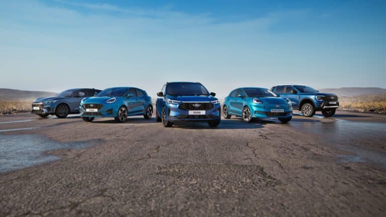 Five blue Ford vehicles, including an electric pickup, are parked in a semi-circle on an empty road under a clear blue sky, with open landscape in the background—showcasing the future of driving with features like Ford Apple Maps integration.