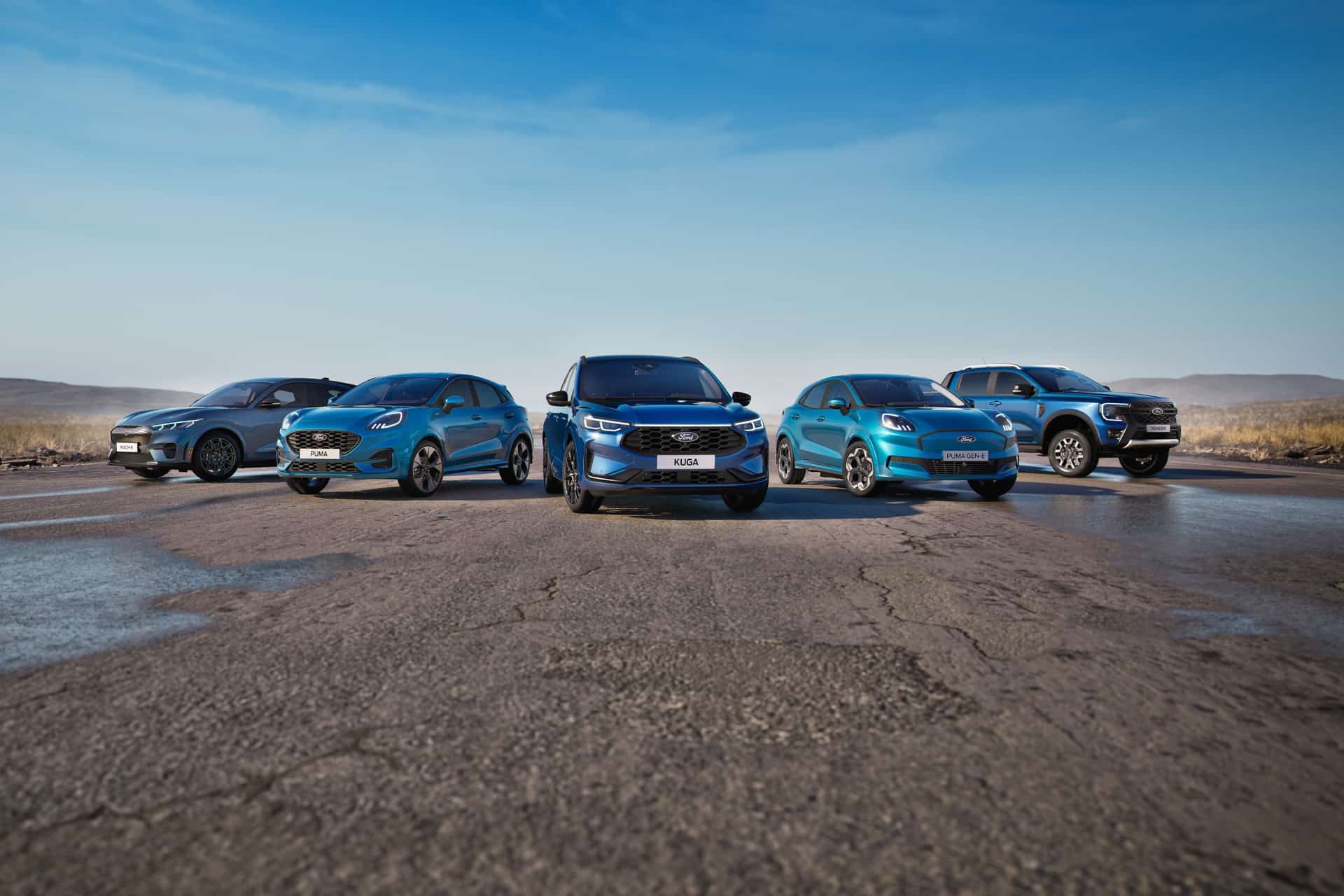 Five blue Ford vehicles, including an electric pickup, are parked in a semi-circle on an empty road under a clear blue sky, with open landscape in the background—showcasing the future of driving with features like Ford Apple Maps integration.
