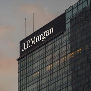 A glass skyscraper with the illuminated "J.P. Morgan" logo near the top, photographed at sunset with a cloudy sky in the background, highlights the firm’s influence on markets like Apple stock and its recent AAPL target announcements.