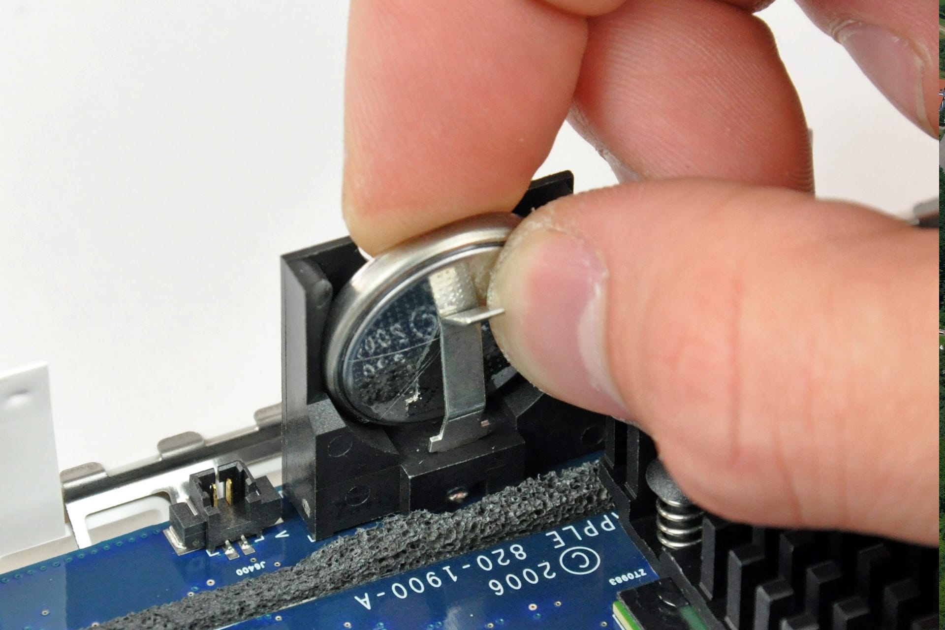 Mac PRAM - A hand is removing a round silver CMOS battery from a holder on a computer motherboard using a small metal tool to perform an NVRAM reset.