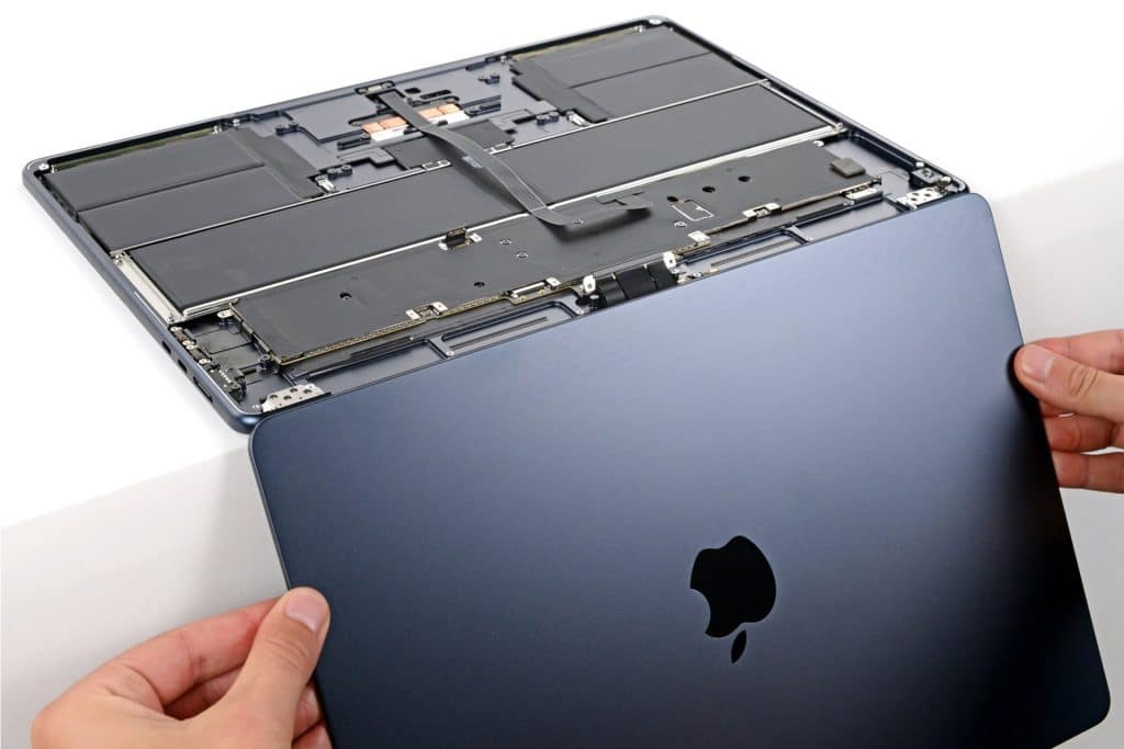 Hands are removing the bottom cover of a dark blue Apple laptop, revealing the internal components, including the battery and circuitry—a closer look that’s often necessary when addressing issues like MacBook Air Flexgate or troubleshooting display problems related to the MacBook Air screen.