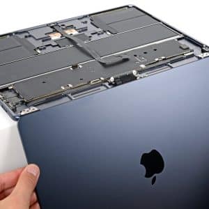Hands are removing the bottom cover of a dark blue Apple laptop, revealing the internal components, including the battery and circuitry—a closer look that’s often necessary when addressing issues like MacBook Air Flexgate or troubleshooting display problems related to the MacBook Air screen.