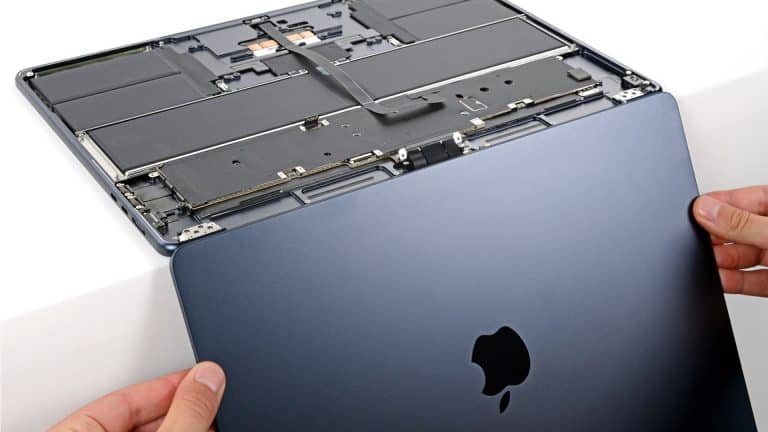 Hands are removing the bottom cover of a dark blue Apple laptop, revealing the internal components, including the battery and circuitry—a closer look that’s often necessary when addressing issues like MacBook Air Flexgate or troubleshooting display problems related to the MacBook Air screen.