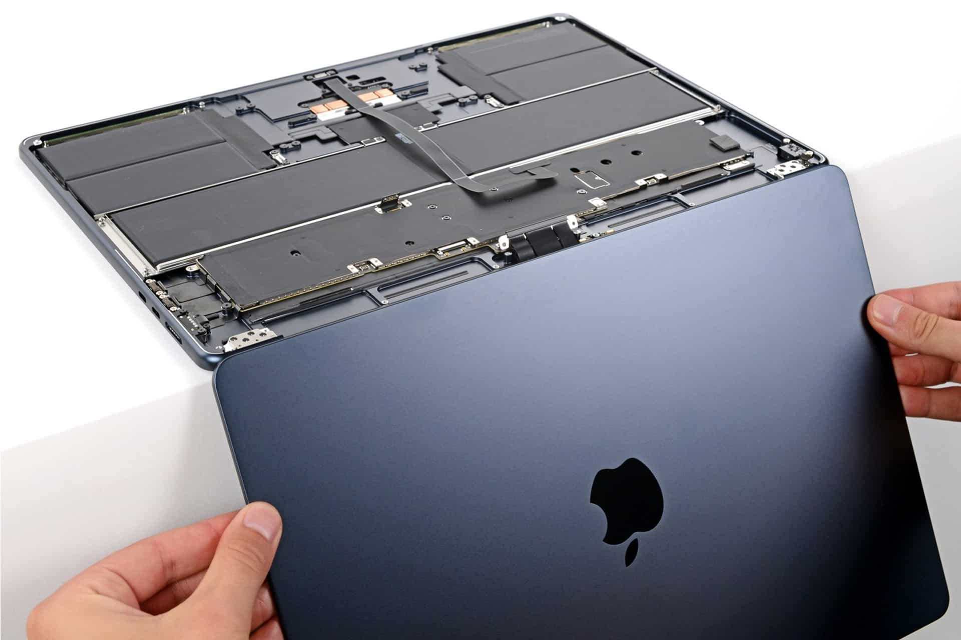 Hands are removing the bottom cover of a dark blue Apple laptop, revealing the internal components, including the battery and circuitry—a closer look that’s often necessary when addressing issues like MacBook Air Flexgate or troubleshooting display problems related to the MacBook Air screen.