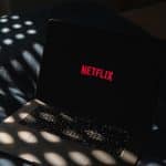 A laptop displaying the red Netflix logo on its screen sits on a dark surface, with patterned light spots shining across the keyboard and background—perfectly capturing the anticipation of diving into the latest streaming lineup.