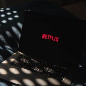 A laptop displaying the red Netflix logo on its screen sits on a dark surface, with patterned light spots shining across the keyboard and background—perfectly capturing the anticipation of diving into the latest streaming lineup.