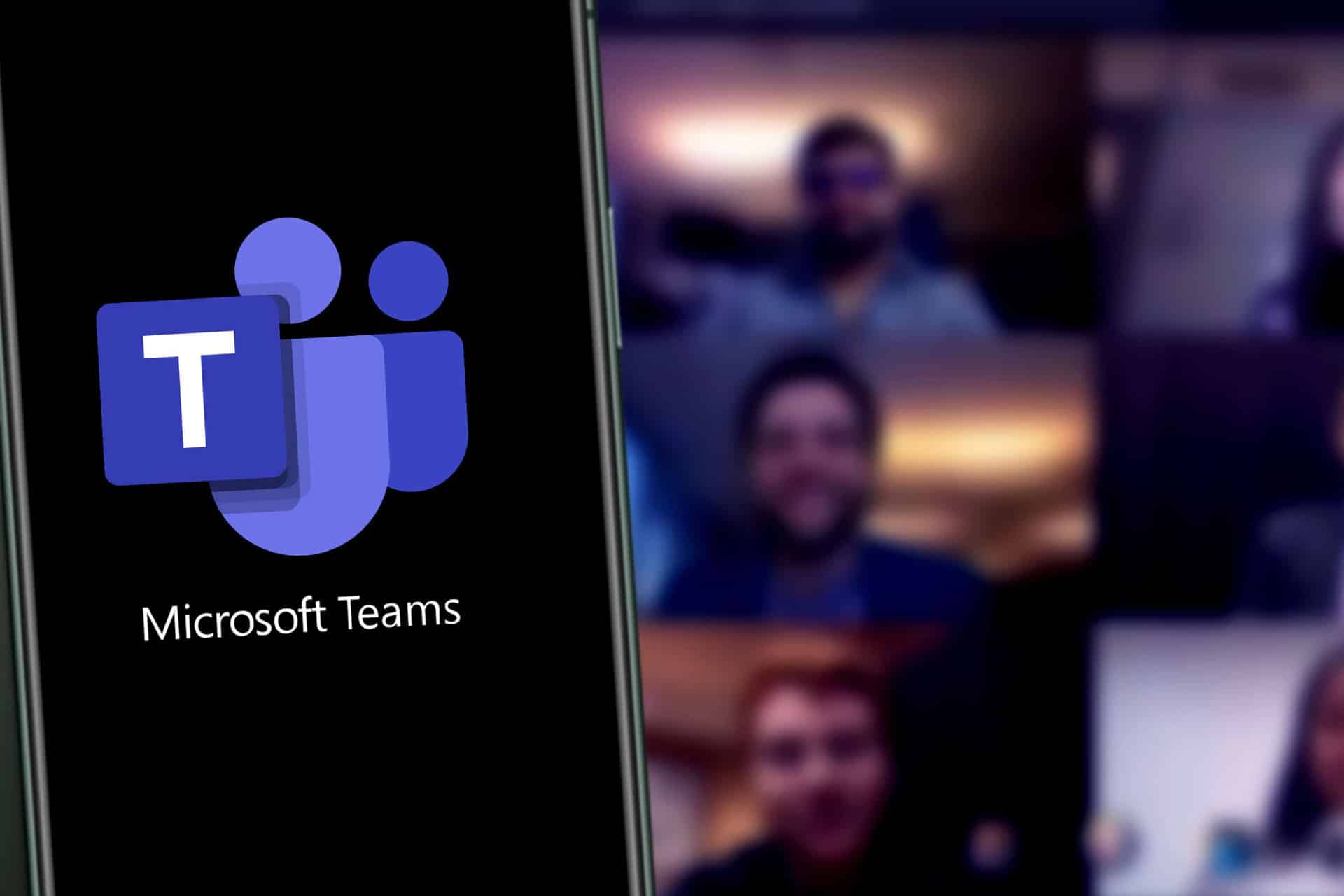A smartphone displays the Microsoft Teams logo, while a blurred video call with multiple participants is visible in the background, highlighting the platform’s popularity for business meetings and video conferencing.