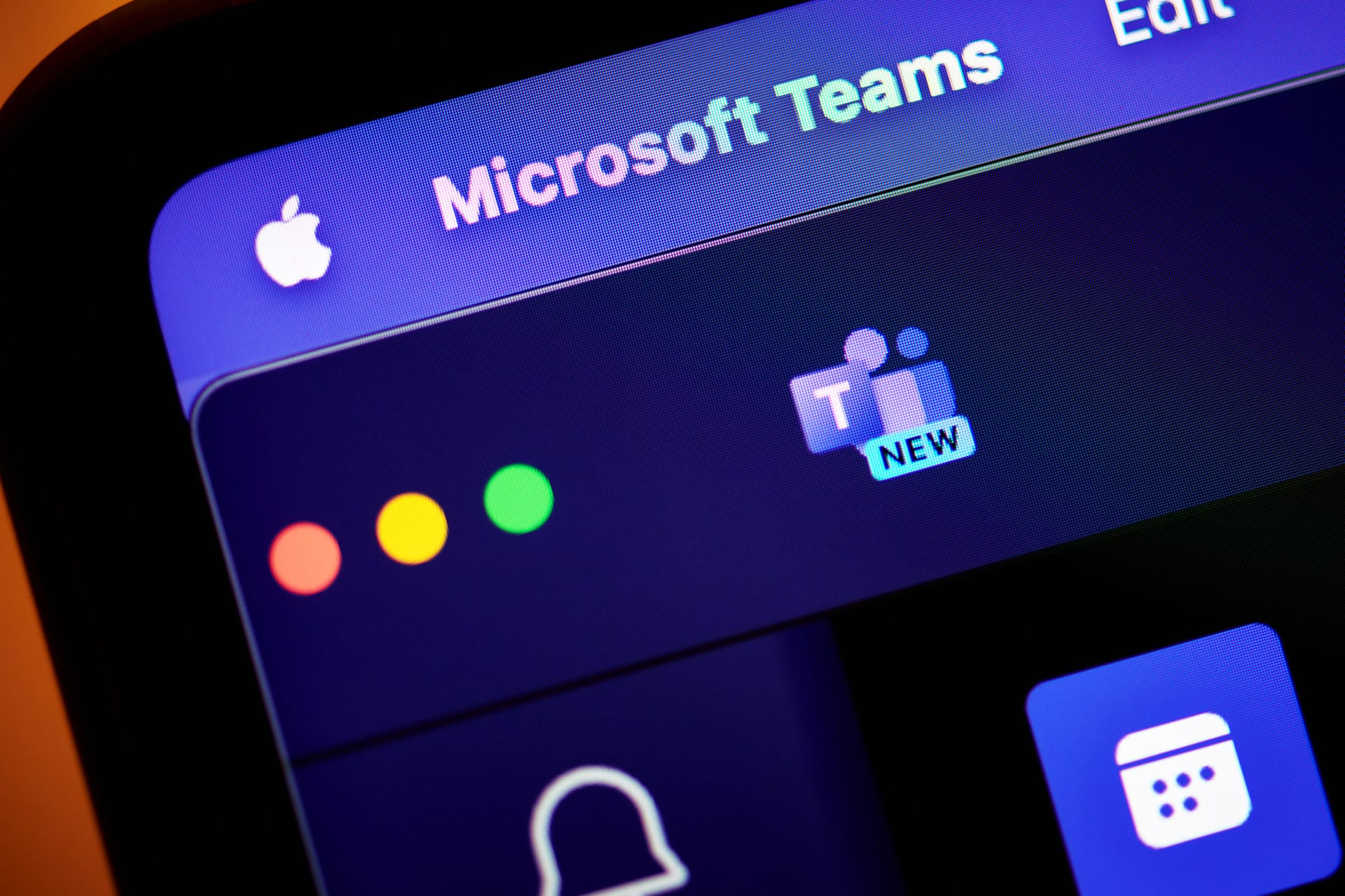 Close-up of a computer screen showing the Microsoft Teams application open on macOS Tahoe, with the Teams icon labeled "NEW" and colorful window control buttons visible at the top left corner. The background features a blank screen, emphasizing the focus on Microsoft Teams.