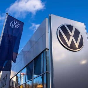 A Volkswagen dealership building with a large VW logo on the exterior wall and a VW flag, set against a blue sky with clouds—perfect for those interested in the latest Volkswagen Car Key features like Apple Wallet compatibility.