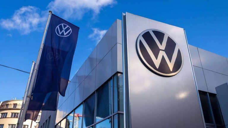 A Volkswagen dealership building with a large VW logo on the exterior wall and a VW flag, set against a blue sky with clouds—perfect for those interested in the latest Volkswagen Car Key features like Apple Wallet compatibility.