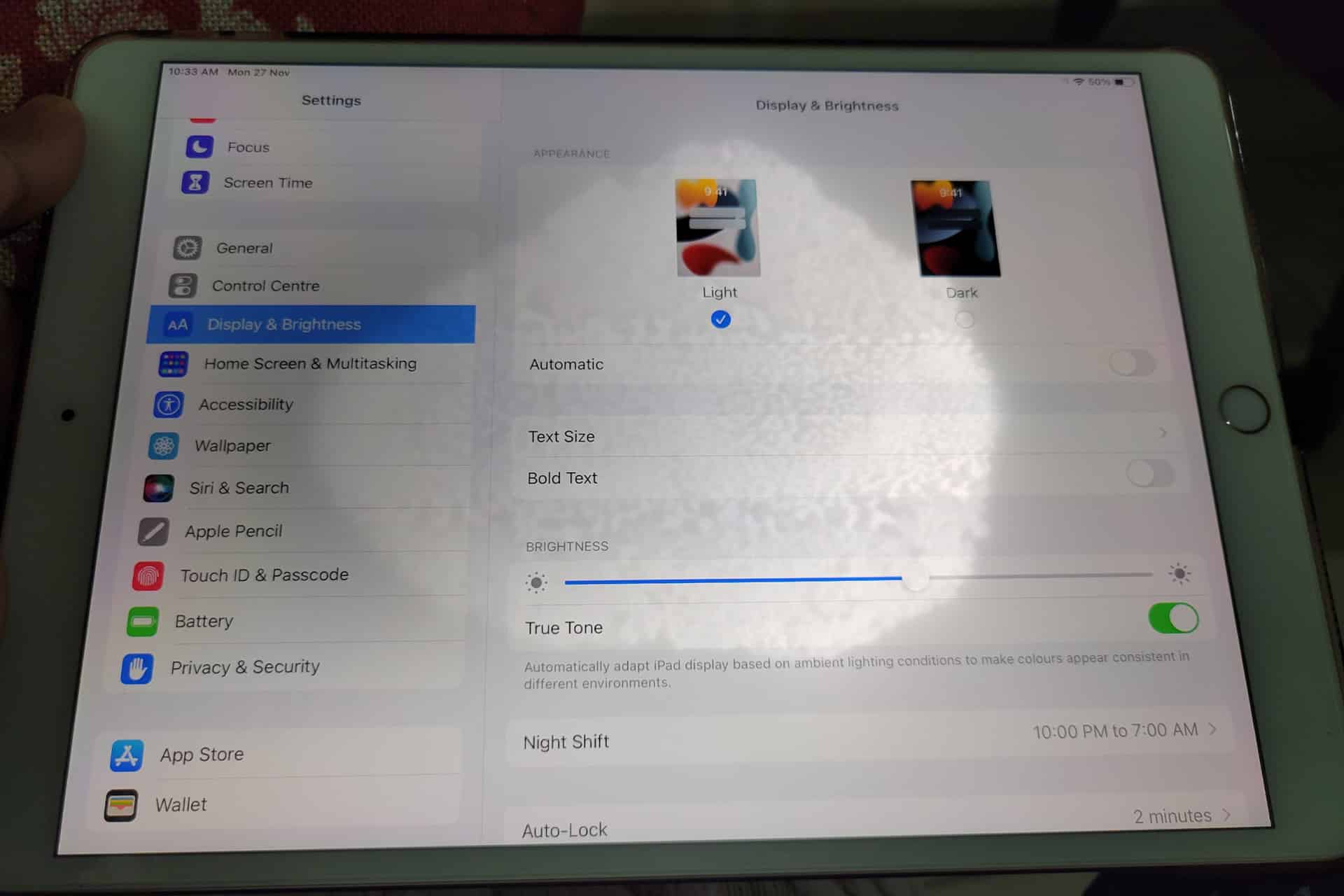 White spot on iPad screen - An iPad displays its "Display & Brightness" settings, showing options for Light and Dark modes, brightness adjustment, True Tone, Night Shift scheduling, and other appearance settings—features that can help users address common issues like an iPad screen problem or an uneven iPad backlight. A hand holds the device.