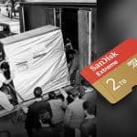 A black-and-white photo shows people moving a large IBM computer; next to it is a color image of a small 2TB SanDisk microSD card, highlighting advances in data storage technology and the remarkable miniaturization that now allows even powerful AI processing on devices like an iPhone.