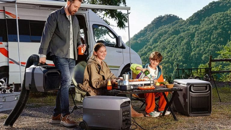 A man, woman, and child enjoy an outdoor meal at a campsite beside a camper van, surrounded by solar generators and mountains in the background, while their iPhone stays charged for capturing memories.