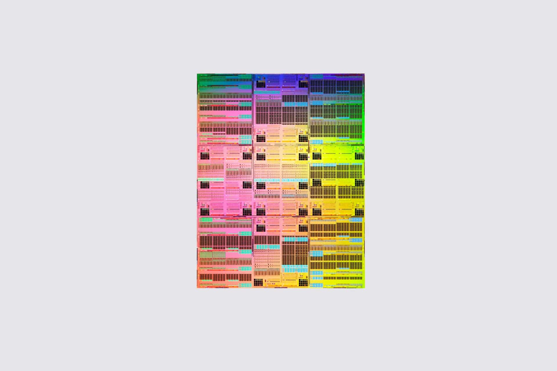 A rectangular computer chip is shown, covered in a grid of tiny, colorful circuits and components, displaying a rainbow-like spectrum from top to bottom. Reminiscent of next-generation Apple Silicon technology and angstrom processors, the intricate surface hints at breakthroughs such as sub-1nm chips. The background is light gray.