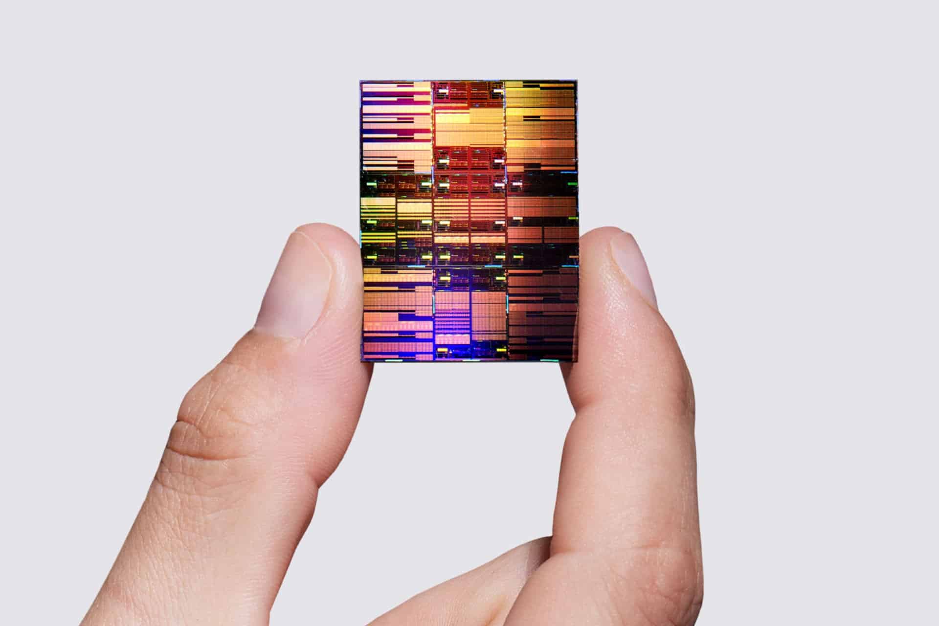 A hand holds a colorful, reflective 0.7nm chip between the thumb and index finger against a plain, light gray background.